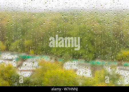 raindrops on glass of home window and blurred city garden on background on rainy autumn day Stock Photo