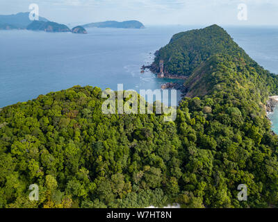 Aerial drone view of a beautiful tropical island with vertical cliffs covered in dense green jungle Stock Photo