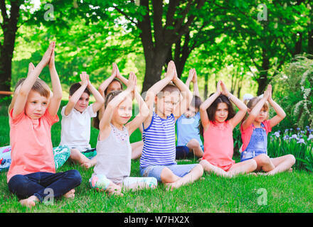 A large group of children engaged in yoga in the Park sitting on the grass. Stock Photo