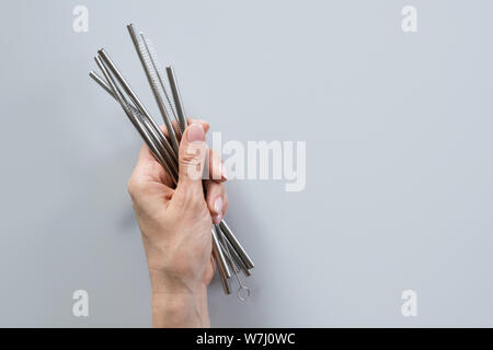 Metallic reusable straws and brush in female hand on grey background. Sustainable lifestyle concept. Zero waste, plastic free. Pollution environment. Stock Photo