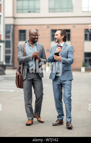 Grey-haired businessman holding smartphone talking to his employee Stock Photo