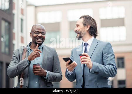 Grey-haired businessman holding smartphone talking to colleague Stock Photo