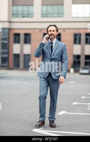 Man wearing grey suit calling colleague while walking by foot Stock Photo