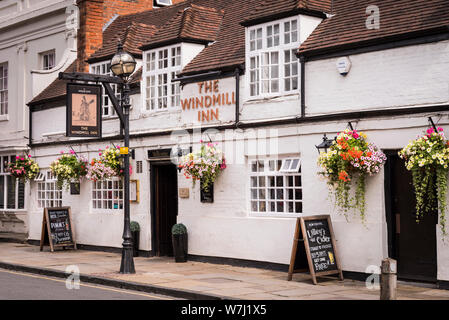 Cafes and restaurants: An exterior view of the Windmill Inn with a hanging sign and flower baskets, and an old fashioned street lamp outside. Stock Photo