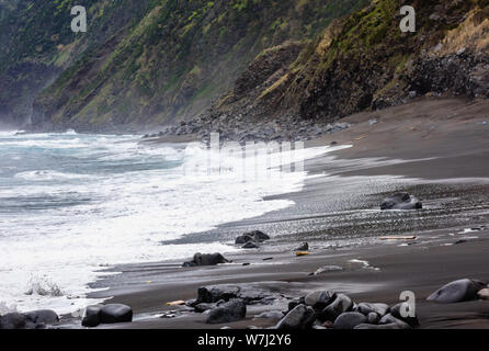 Ocean waves splashing on wet beach near steep cliffs, in Azores, Portugal. Stock Photo