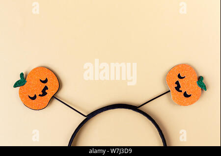 Halloween party accessory, rim with two shiny pumpkins with cute creepy faces. Pastel yellow background, place for text. Holiday flat lay. Minimal sty Stock Photo