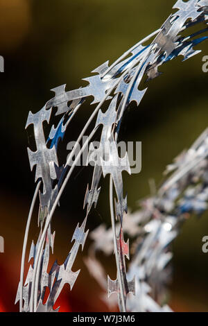 Twisted barbed wire like blades on a beautiful colored background. Blurred red background with green. Selective focus on the fence. Stock Photo