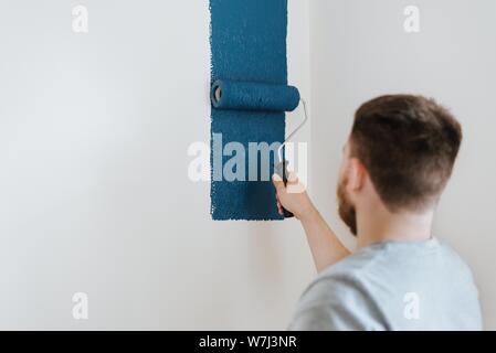 White caucasian male painting a white wall with blue color Stock Photo