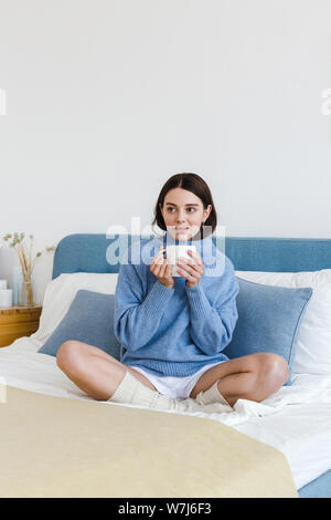 Girl in a blue sweater in interior Hygge style with a cup in hand sits on the bed Stock Photo