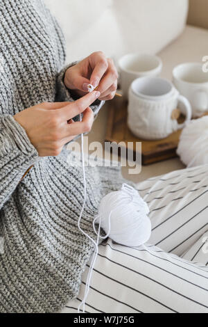 girl in a warm gray sweater knits sitting on a sofa in a cozy interior hygge Stock Photo