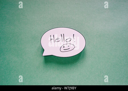 Speech bubble sign with the words Hello and Smiley. Speech message symbol on paper green background. Greeting card or invitation. Stock Photo