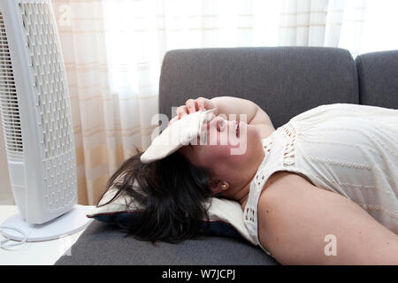 Woman with an ice pack lays in front of the fan at home on a hot day Stock Photo