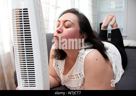 Woman kisses the cold breeze blowing in her face from her at home fan Stock Photo