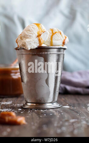 Vanilla ice cream with salted caramel sauce in a frosted container over a wood background . Selective focus with blurred background. Top View. Overhea Stock Photo