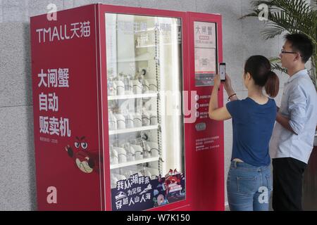 A Chinese customer uses her smartphone to scan the QR code on a vending machine to buy hairy crabs at the headquarters of Yiguo Fresh Food, an Alibaba Stock Photo