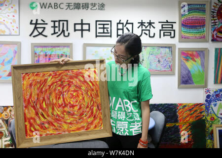 A volunteer shows a colorful painting created by a child with mental and intellectual disabilities as a part of a charity project titled 'Enlighten Li Stock Photo