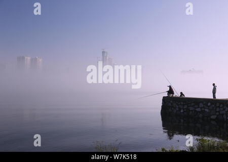 Citizens fishing along the Hanjiang River look at the high-rise buildings and skyscrapers seen vaguely as a mirage appears in Xiangyang city, central Stock Photo