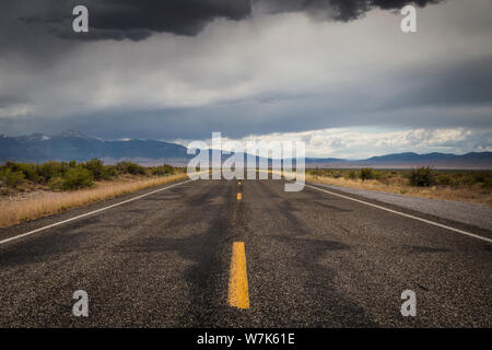 The yellow lines of a two lane highway, US Highway 50, under overcast skies in the middle of the high desert at the Utah Nevada border on a summer aft Stock Photo