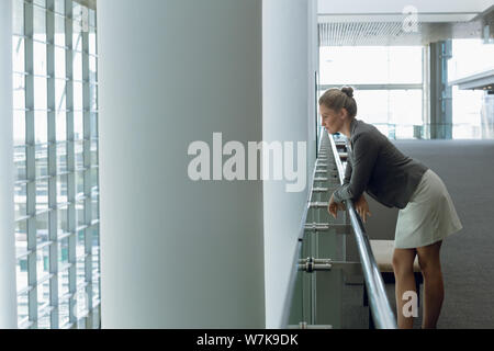 Thoughtful Businesswoman leaning on railing in the corridor Stock Photo