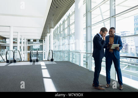 Two businessmen stand using tablet in office lobby Stock Photo