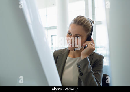 Businesswoman talking on headset at desk in office Stock Photo
