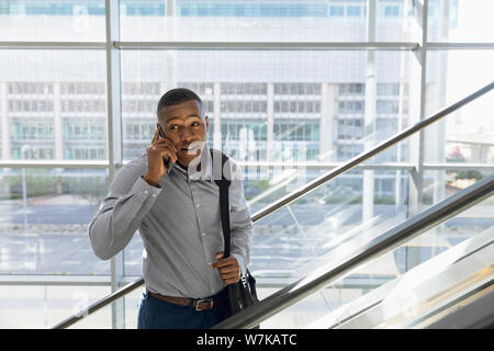 Young businessman talking on phone on an escalator Stock Photo