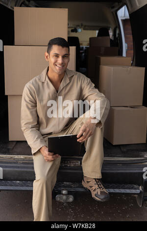 Delivery man with clipboard looking at camera outside the warehouse Stock Photo
