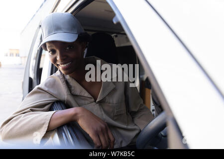 Delivery woman looking at camera while sitting in front seat of van outside the warehouse Stock Photo