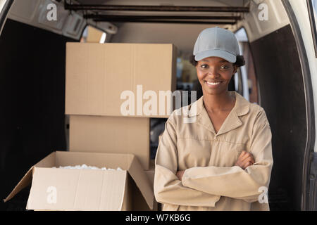Delivery woman standing with arms crossed and looking at camera near van outside the warehouse Stock Photo