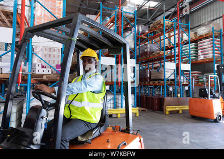 Male worker looking at camera while driving forklift in warehouse Stock Photo