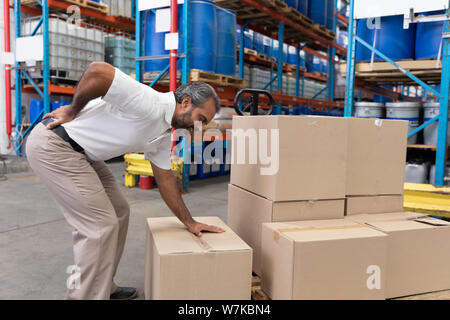 Male staff suffering from back pain while holding heavy cardboard box Stock Photo