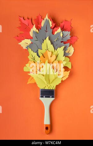 Top view on flat lay with brush loaded with paint made from paper Autumn leaves on orange paper background. Concept home renovation background in red,