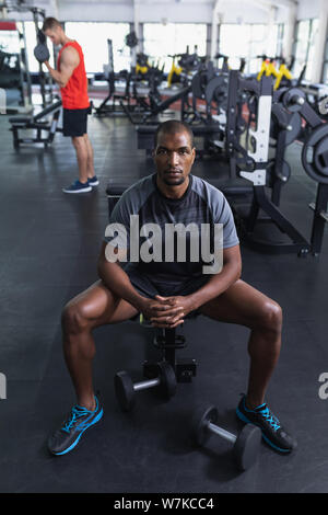 Fit man relaxing with hands clasped on bench in fitness center Stock Photo