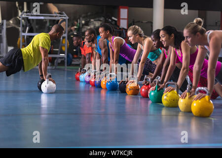 Male trainer training women to perform exercise with kettlebell Stock Photo