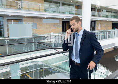 Businessman on smartphone going up escalator Stock Photo