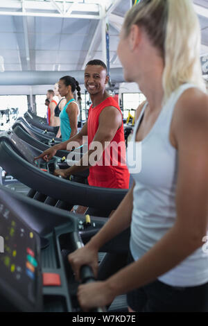 Fit man interacting with woman while exercising on treadmill Stock Photo