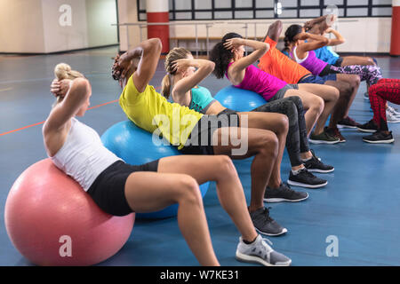Female trainer training people to perform yoga on exercise ball Stock Photo