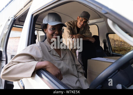 Delivery man and woman looking at camera while sitting in van outside the warehouse Stock Photo