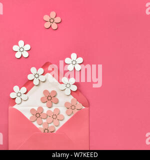 Springtime flat lay on pink paper with decorative wihte and peach colored flowers flying from open envelope. Paper background in coral color, square c Stock Photo