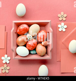 Easter flat lay in coral color with painted eggs, greeting cards, envelopes and decorative flowers, square composition Stock Photo