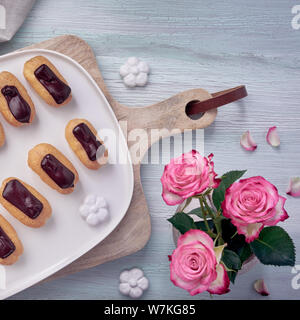 Mini vanilla eclairs with chocolate frosting on light textured background, top view, square composition Stock Photo