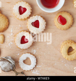 Top view of traditional Linzer cookies filled with strawberry jam on wooden board with heart-shaped openings. Valentine's day or Christmas concept. Stock Photo
