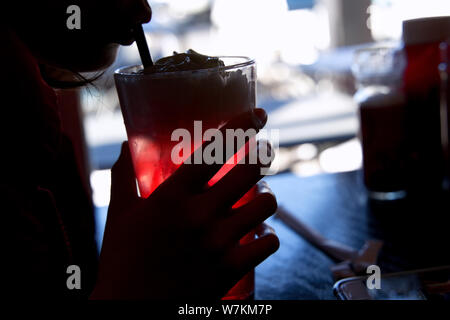 Silhouette of an ice cold cherry soda float in the hands of a young customer looking at her cellphone. Stock Photo