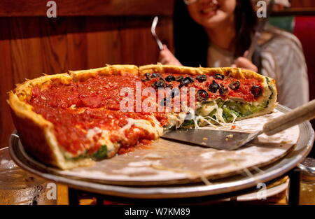 A Chicago style deep dish pizza being eaten by hungry and smiling customers. Stock Photo