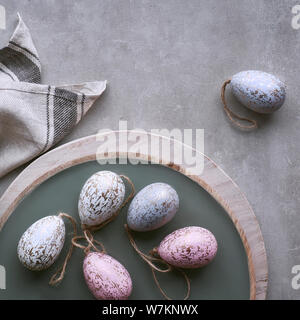 Top view of decorative Easter eggs in pastel colors on decorative tray with linen towel on light stone background, square composition Stock Photo