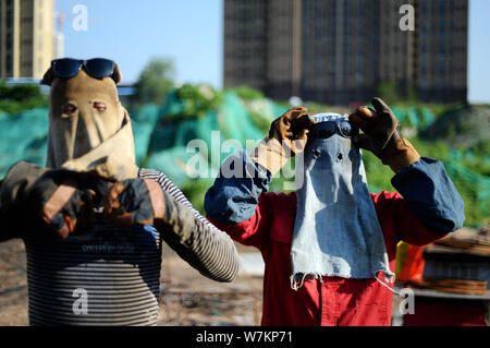 Chinese workers wearing masks and gloves make steel reinforcement cages, part of a building's foundation, on a scorching day at a construction site in Stock Photo