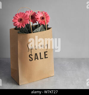 Coral gerbera daisy flowers and craft papper shopping bags on green paper background, square composition, Springtime sale concept image with text "Spr Stock Photo
