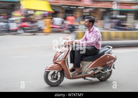 An Indian man riding his scooter in downtown Varanasi on a late afternoon Stock Photo