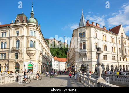 Tourists crossing the famous triple bridge towards the old town and Ljubljana castle on Castle hill above the Old town Ljubljana Slovenia EU Europe Stock Photo