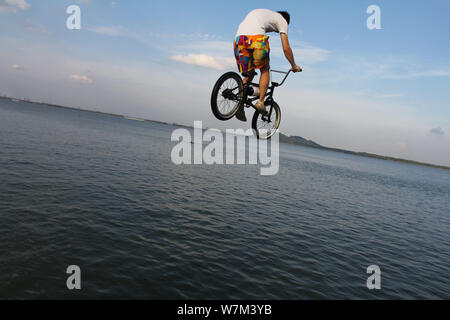 A BMX (Bicycle Motocross) rider jumps into the East Lake to cool off amid hot weather from a plank road during the 'Lake-jumping' festival in Wuhan ci Stock Photo